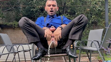 Un hombre de traje con el pene enjaulado se toca el ano y se mea en público con calcetines transparentes